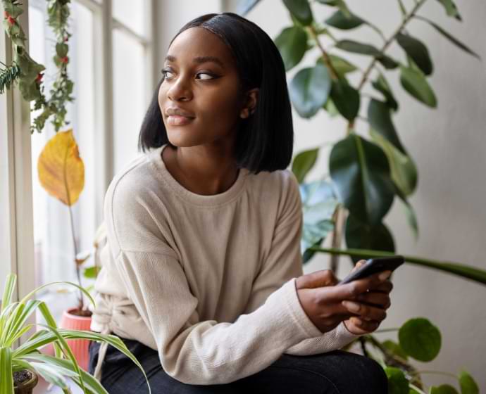 Mulher olhando pela janela enquanto segura um celular